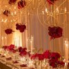 دیزاین میز جشن عروسی با گل های رز قرمز و شمع همراه با گل آرایی لوسترهای طلایی