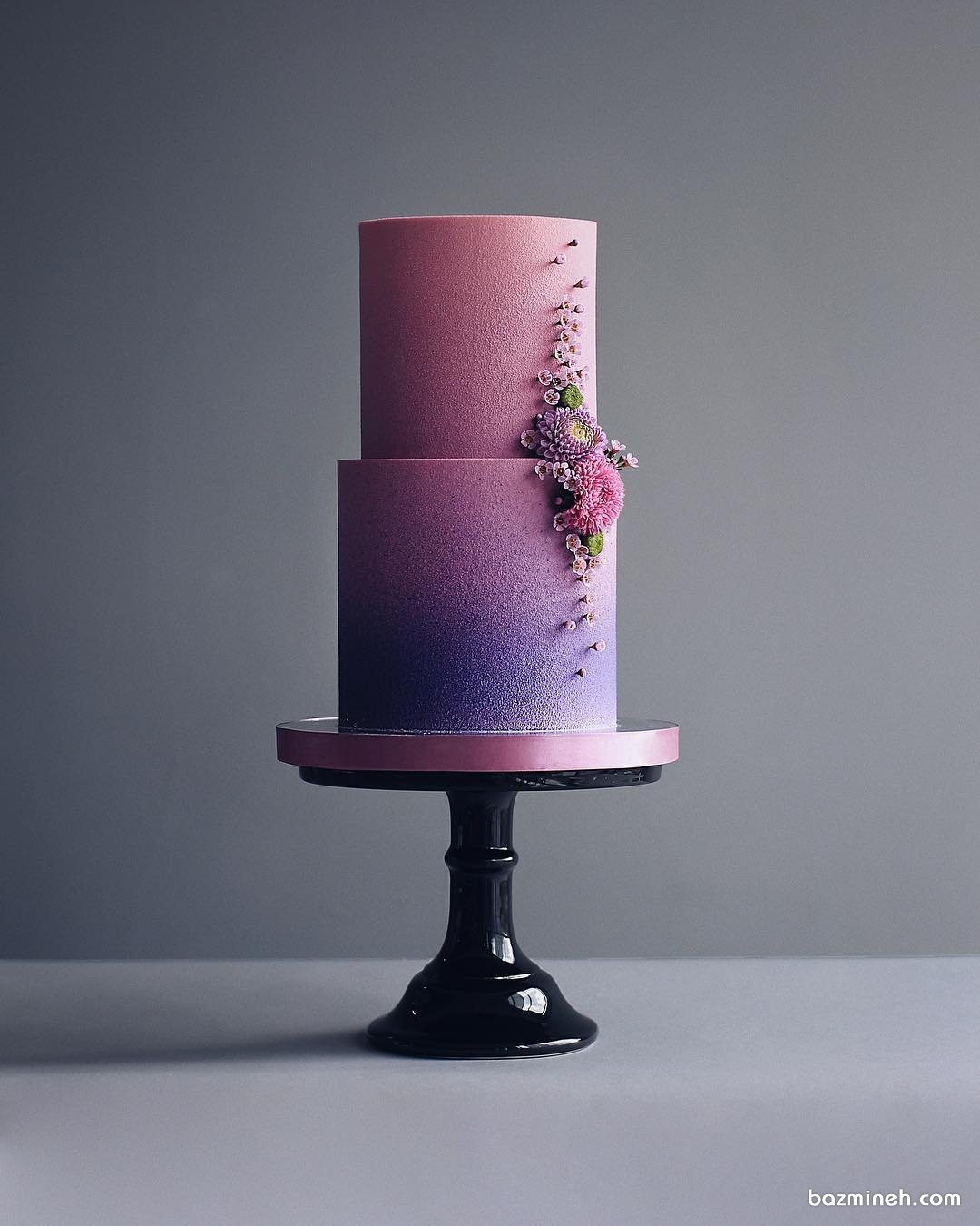 کیک خاص دوطبقه جشن تولد تزئین شده با گل های طبیعی با تم صورتی بنفش